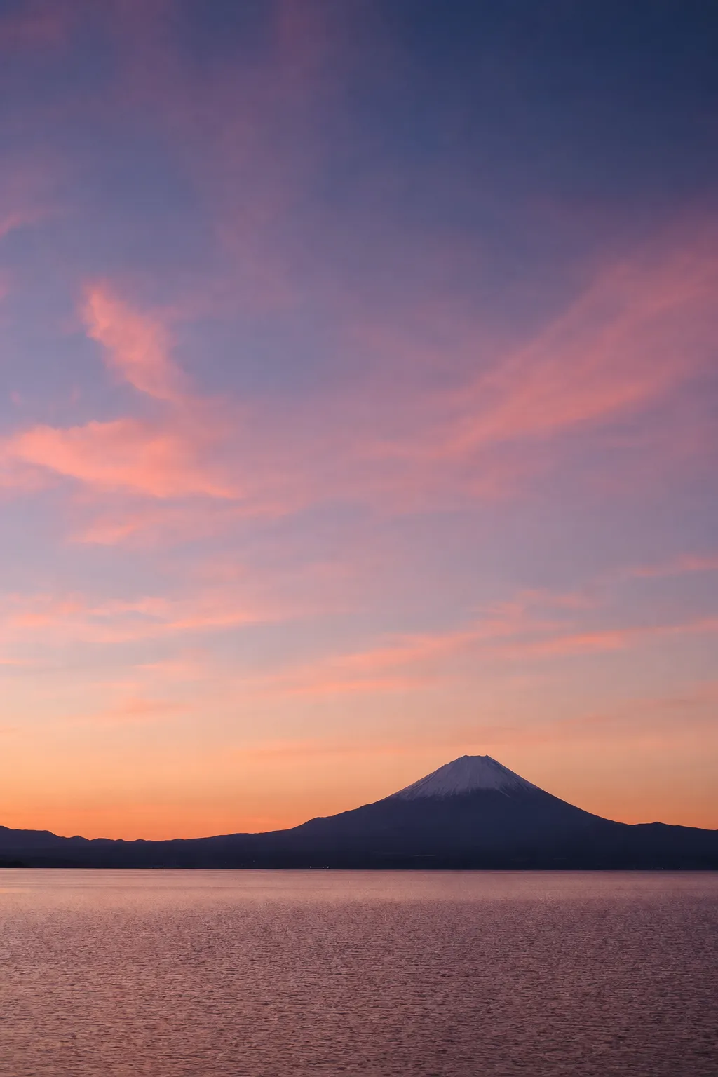 夜明けの珊瑚色に染まる空と、富士山を望む静かな湖
